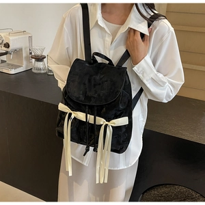 Detail view of black suede backpack featuring a white satin bow and MIKA embossed flap