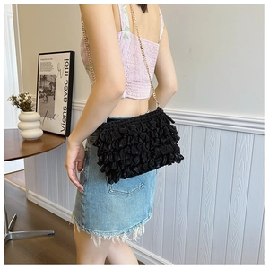 Detail of ruffled black satin crossbody bag with a delicate gold metal chain strap