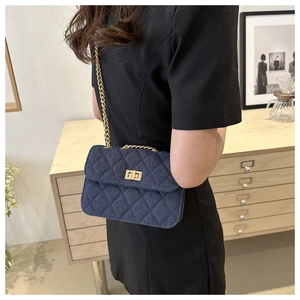 Detail of dark blue denim crossbody bag with quilted texture and gold chain strap