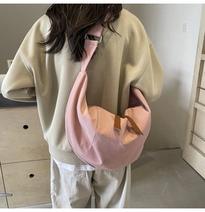 Pink canvas half-moon crossbody bag shown on a model in a minimalist interior setting