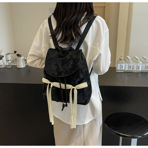 Detail of a vintage black PU backpack with cream ribbons and Nika embossed logo on the flap