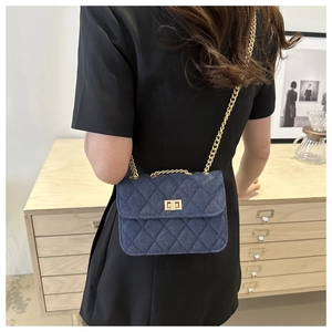 Detail view of a blue quilted denim crossbody bag with gold chain strap on a model