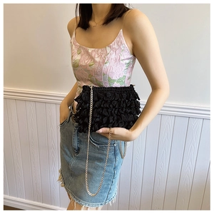 Detail of black pleated fabric crossbody bag with elegant gold chain strap on model