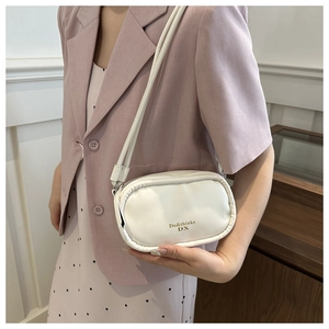 Detail of white PU leather crossbody bag with gold Do&thinks DX logo on elegant pink suit