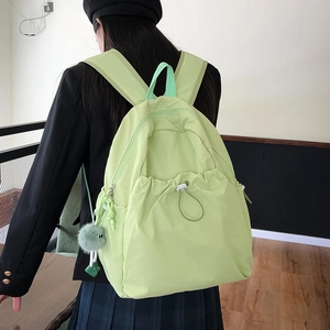 Dettaglio dello zaino in nylon verde chiaro con tasca a coulisse e pompon in peluche