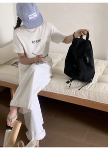 Black nylon backpack detail showing flap structure and side zipper on a model