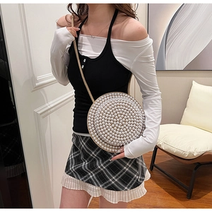 Dettaglio di una borsa rotonda in tessuto intrecciato con decorazione di perle bianche
