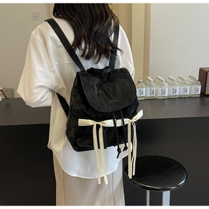 Close-up of black velvet backpack featuring white satin bows and embossed NiKa logo detail
