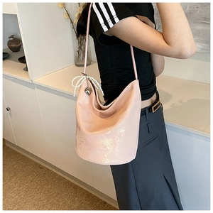 Detail of pink PU leather bucket bag featuring pearl bow and metal heart charm on model