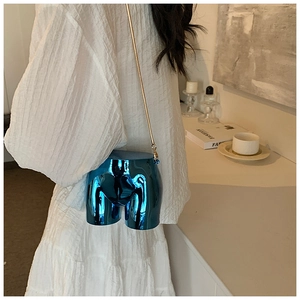 Detail of artistic blue metallic crossbody bag with gold chain on model in warm interior
