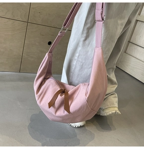 Pink crescent crossbody bag with brown leather lace details and adjustable strap