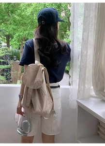 Minimalist beige nylon drawstring backpack shown in a natural outdoor lifestyle setting