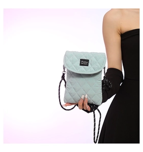 Detail of mint green quilted crossbody bag with woven polka dot strap and fashion tag
