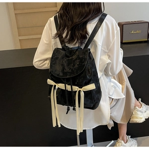 Detail of a vintage black PU backpack with crinkled texture and beige ribbon bows