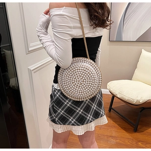 Dettaglio di una borsa a tracolla rotonda con perle sintetiche bianche e tracolla sottile