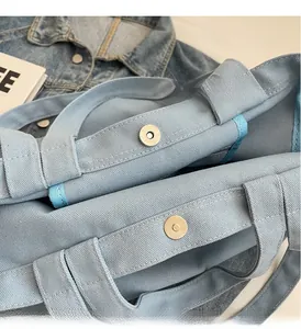 Detailed macro view of the metal magnetic clasp on a light blue canvas tote bag
