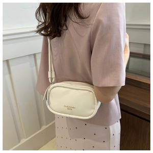 Detail of white PU leather crossbody bag with gold lettering and slim shoulder strap