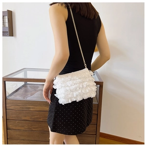 Close-up of white ruffled crossbody bag with a delicate gold chain strap on a model