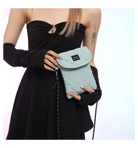 Detail of light mint green quilted crossbody bag with black rope strap and fashion label