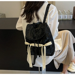 Detail of black faux leather backpack featuring two large cream satin bows and logo