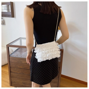 Detailed view of white ruffled crossbody bag with gold chain strap worn by a model