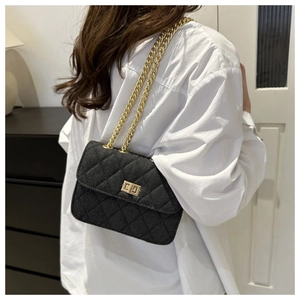 Detail of black quilted denim crossbody bag with gold chain strap worn by a model