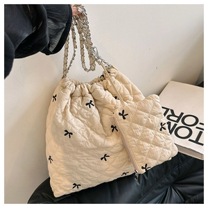 Beige quilted tote bag with black bow embroidery and silver chain strap details