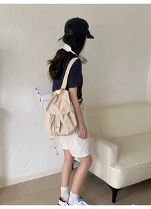 Rear view of a model wearing the minimalist beige nylon drawstring backpack in a soft setting