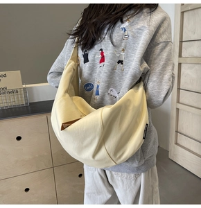 Canvas crescent crossbody bag worn by model featuring side woven label and leather zip puller