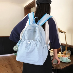 Dettaglio dello zaino in nylon azzurro con coulisse bianca e ciondolo mostro di peluche verde