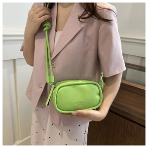 Side view of a mint green mini PU leather crossbody bag worn with a pink blazer