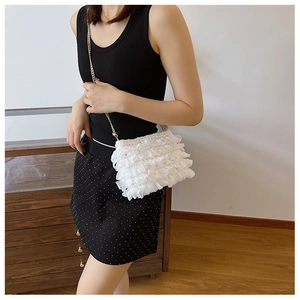 Macro detail of white ruffled fabric shoulder bag with metallic chain strap for women