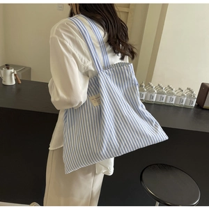 Detail of blue and white striped canvas tote bag worn by a model in a modern interior