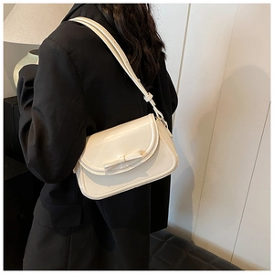 Dettaglio borsa a spalla in pelle PU crema con fiocco indossata su un blazer nero chic