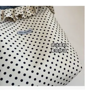 Detail of polka dot fabric bag showing ruffled edge and gray woven label with brand text