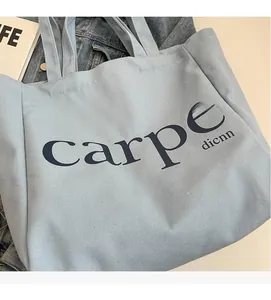 Detail of light blue canvas tote bag with black carpe print on soft white surface