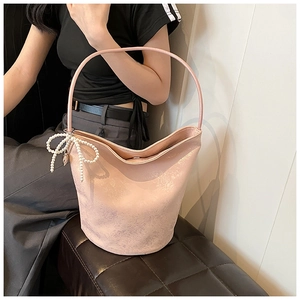 Detail of light pink PU bucket bag with pearl bow charm worn by a model in soft light