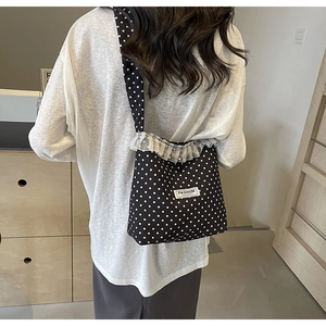 Detail of black polka dot canvas bag featuring white lace trim and fashion logo tag