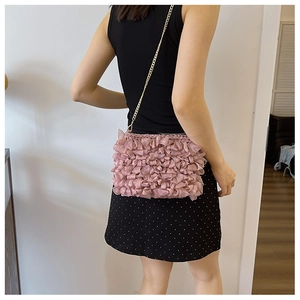 Detail of pink pleated fabric shoulder bag with elegant gold chain strap and petal texture