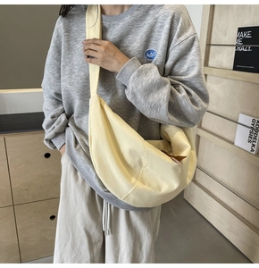Detail of a large pale yellow crescent canvas crossbody bag worn in a casual setting
