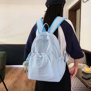 Dettaglio zaino in nylon azzurro con coulisse bianche e portachiavi in peluche verde
