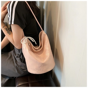 Detail view of pink pearlescent PU leather underarm bag with white pearl bow charm