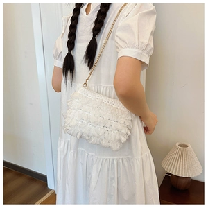 Detailed view of a white ruffled fabric crossbody bag with a delicate gold chain strap