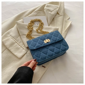 Blue denim quilted chain crossbody bag with gold hardware on white blazer background