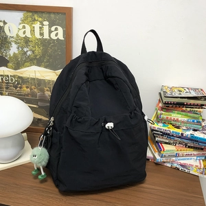 Dettaglio dello zaino in nylon nero con tasca frontale a coulisse e ciondolo verde