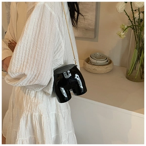 Detail of unique torso-shaped crossbody bag in black patent leather with gold chain