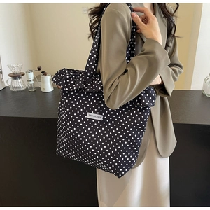 Close-up of stylish black polka dot tote bag with ruffle trim and textile logo label