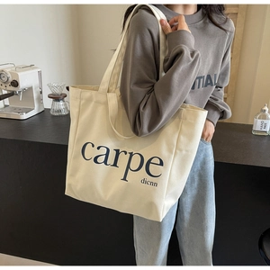 Detail of a minimalist cream canvas tote bag featuring carpe text worn by a model