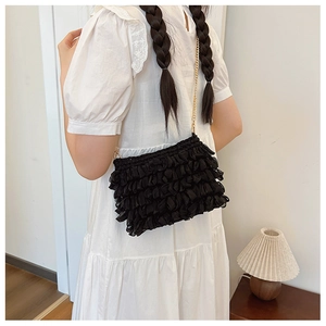 Detailed view of a black ruffled crossbody bag with a delicate gold chain strap