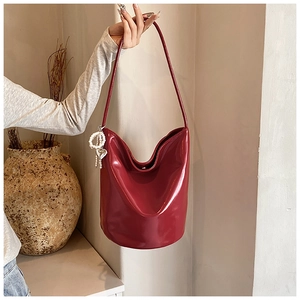 Close-up of glossy wine red PU leather shoulder bag with decorative pearl heart charm